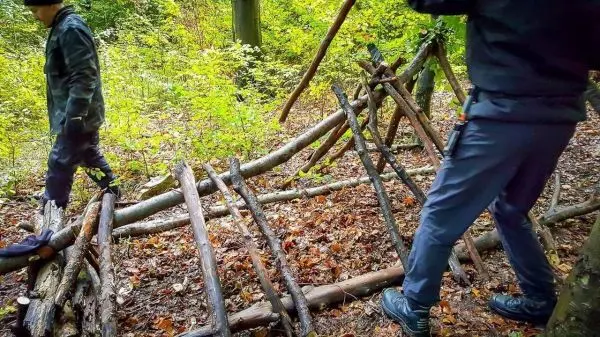 Zwei Personen bauen eine Holzkonstruktion aus Ästen im Wald