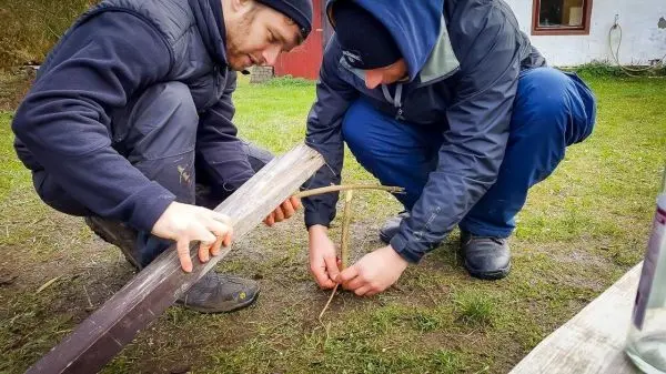 Zwei Personen bauen eine Konstruktion aus Holz und Ästen