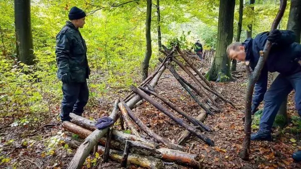 Zwei Personen bauen eine Laubhütte aus Ästen im Wald