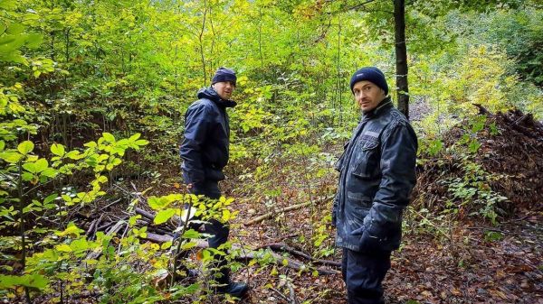 Zwei Personen stehen in einem bewaldeten Gebiet zwischen Bäumen und Sträuchern