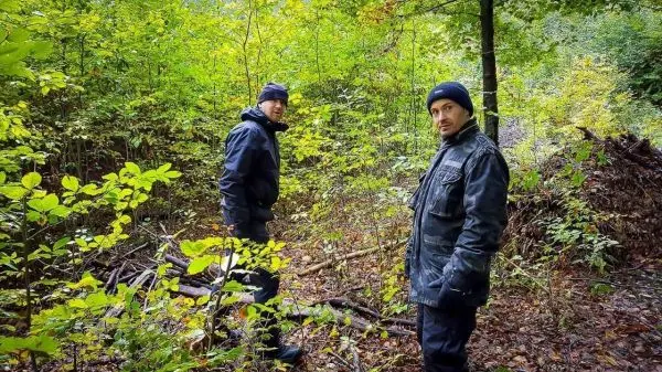 Zwei Personen stehen in einem bewaldeten Gebiet zwischen Bäumen und Sträuchern