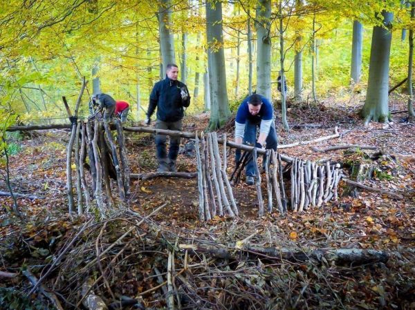 Drei Personen bauen eine Holzkonstruktion aus Ästen im Wald