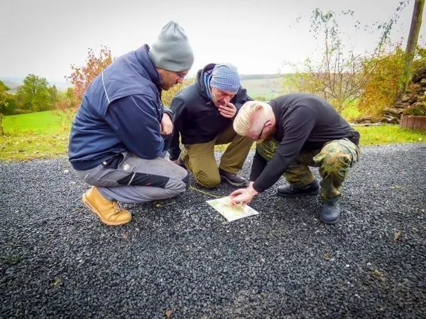 Drei Personen betrachten gemeinsam eine Karte auf dem Boden