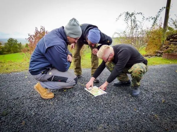 Drei Personen betrachten gemeinsam eine Karte auf dem Boden