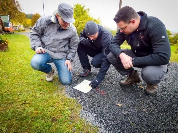 Drei Personen betrachten gemeinsam eine Karte auf einem Kiesweg