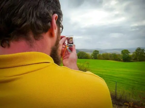 Ein Kompass wird auf eine Landschaft mit Wiesen und Hügeln ausgerichtet