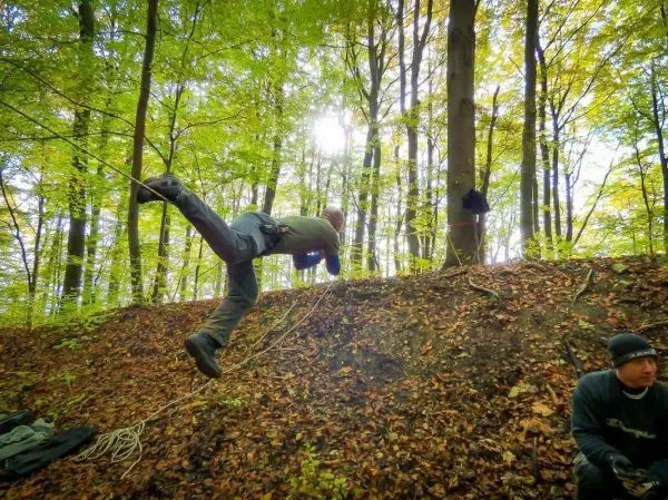 Ein Mann schwingt an einem Seil über einen Hang im Wald
