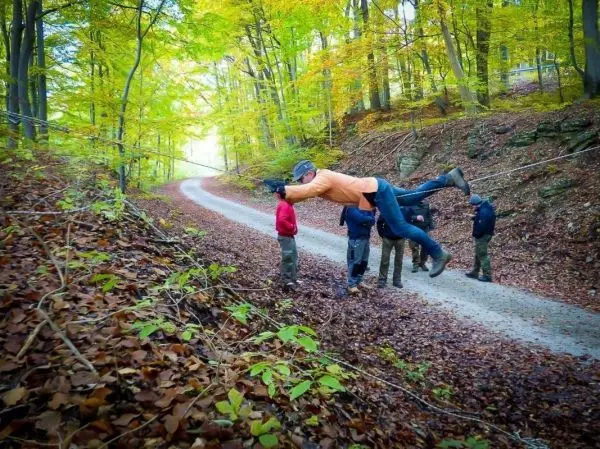 Ein Mann schwingt an einem Seil über einen Waldweg, während andere zuschauen