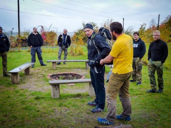 Ein Teilnehmer erhält eine Anleitung zur Ausrüstung von einem Trainer am Lagerfeuer