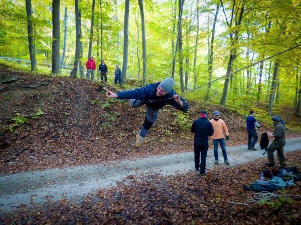 Ein Teilnehmer schwingt an einer selbstgebauten Seilbrücke über einen Waldweg