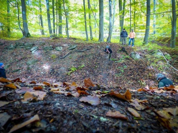 Eine Person springt von einem Hang in einen Wald mit Laub und Felsen