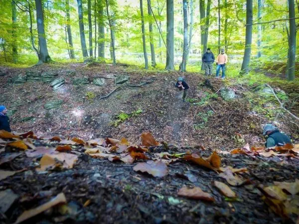 Eine Person springt von einem Hang in einen Wald mit Laub und Felsen