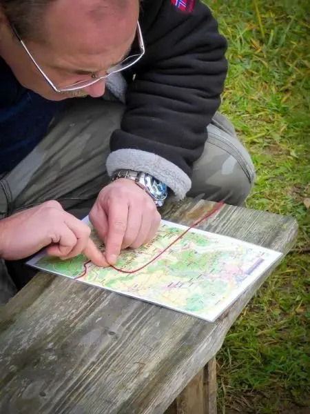Finger zeigt auf eine Karte, während auf einer Holzbank gesessen wird