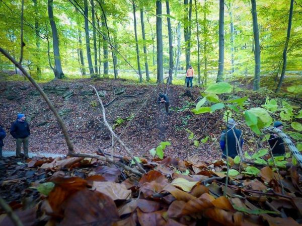 Gruppe steht an einem Hang im Wald, einige beobachten einen anderen Teilnehmer