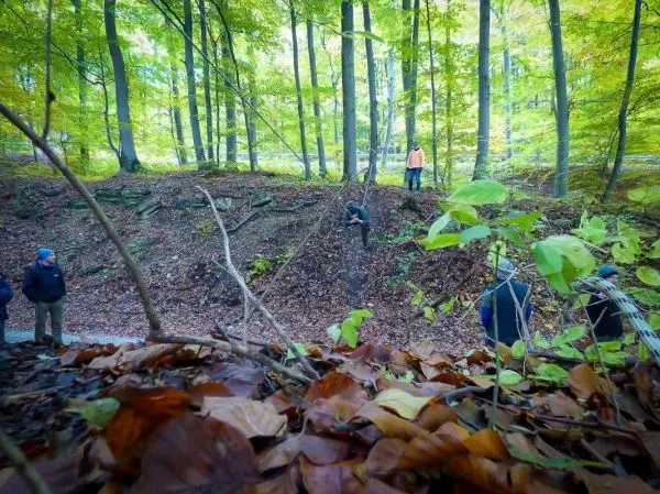 Gruppe steht an einem Hang im Wald, einige beobachten einen anderen Teilnehmer