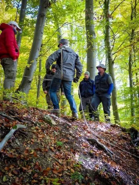 Gruppe steht an einem Hang im Wald und diskutiert über die Umgebung