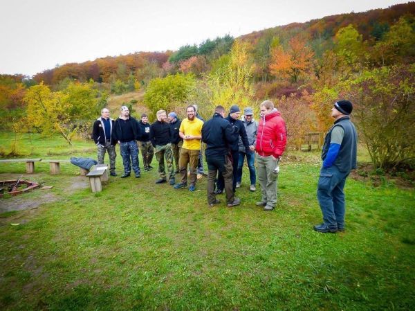 Gruppe steht auf einer Wiese und diskutiert um ein Feuerstelle