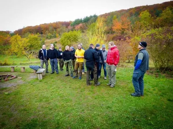Gruppe steht auf einer Wiese und diskutiert um ein Feuerstelle
