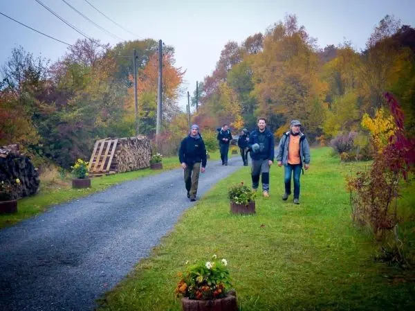 Gruppe von Personen geht einen Schotterweg entlang, umgeben von Bäumen und Holzstapeln
