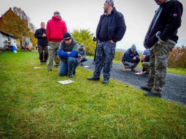 Gruppierung von Personen auf einer Wiese, einige knien und betrachten Unterlagen
