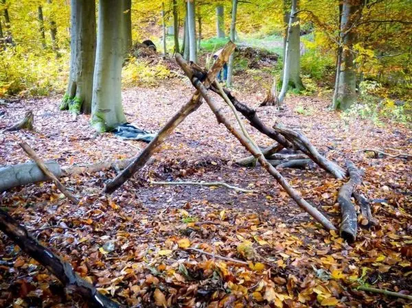 Holzkonstruktion für eine Tarp-Notunterkunft zwischen Bäumen im Laub