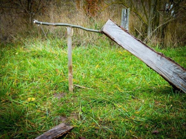 Holzplatte ist schräg auf einem Pfahl gelagert, mit einem Stab als Unterstützung
