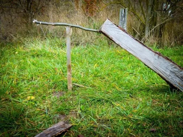 Holzplatte ist schräg auf einem Pfahl gelagert, mit einem Stab als Unterstützung