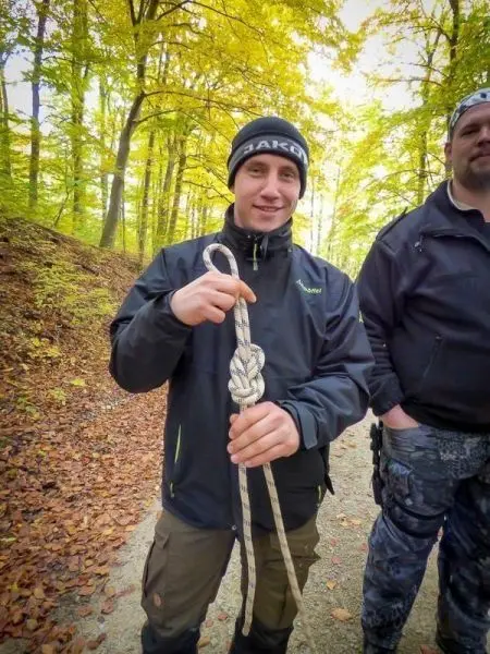 Kletterseil mit Knoten in der Hand gehalten, im Hintergrund herbstliche Baumlandschaft