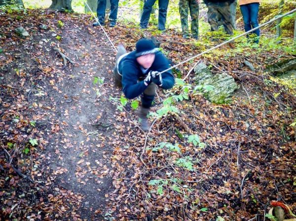 Kriechender Teilnehmer nutzt Seil zur Überwindung eines steilen Hangs im Wald