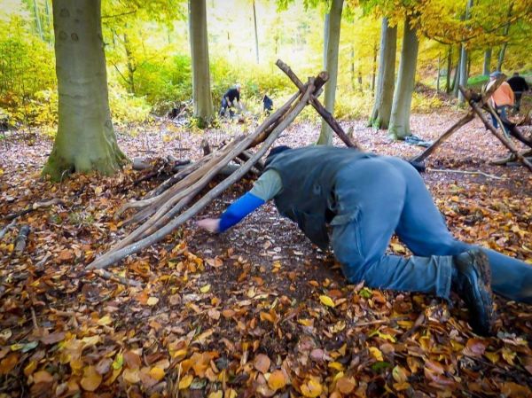 Kriechender Teilnehmer unter einer improvisierten Tarp-Notunterkunft aus Ästen