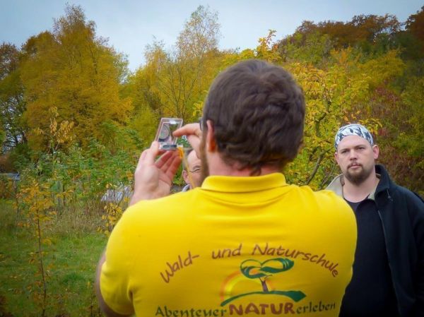 Mann hält Kompass in der Hand und zeigt ihn einer Gruppe im Wald