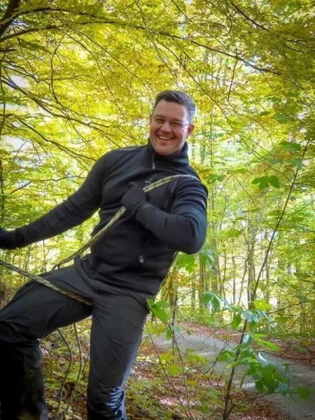 Mann hält sich an einem Seil und lächelt in einem Wald