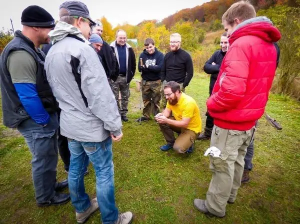 Mann in gelbem Shirt demonstriert Technik auf dem Boden, umringt von Teilnehmern