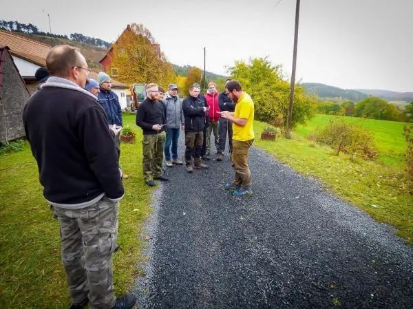 Mann in gelbem Shirt erklärt einer Gruppe auf einem Schotterweg etwas