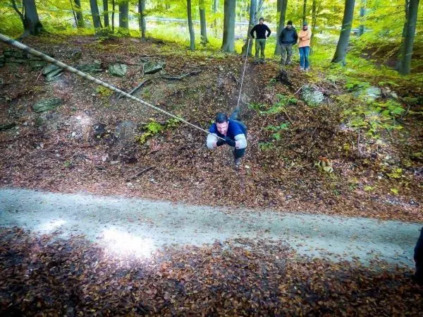 Mann überquert mit Seil eine steile Böschung im Wald