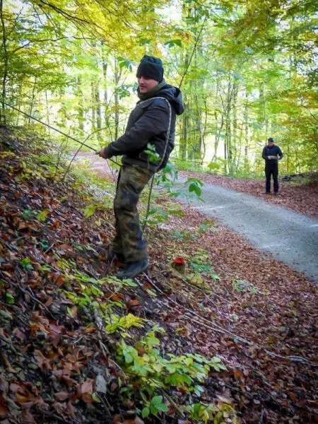 Mann zieht eine Schnur an einem Hang entlang, während ein weiterer Mann im Hintergrund steht
