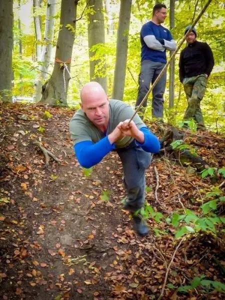 Mann zieht sich an einem Seil eine Steigung hinauf, während andere zuschauen