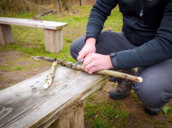 Messer schält Rinde von einem Stock auf einer Holzbank