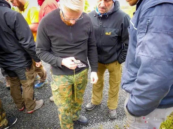 Person betrachtet Kompass, umgeben von anderen Personen beim Überlebenstraining