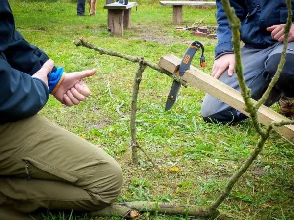 Person bindet einen Stock mit Schnur zusammen beim Überlebenstraining