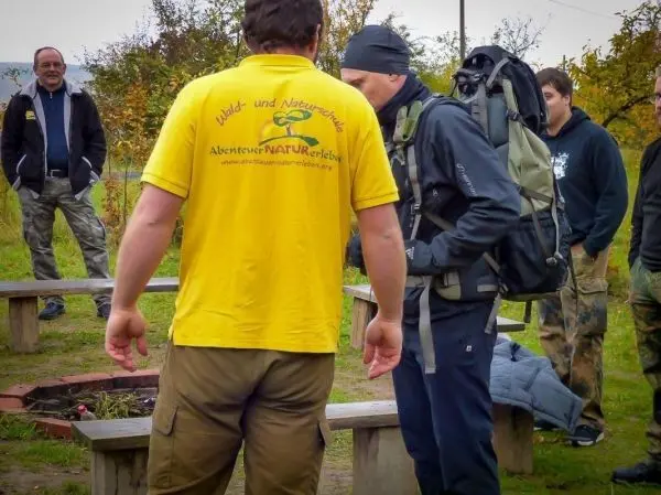 Person mit Rucksack spricht mit anderer Person im Freien beim Überlebenstraining
