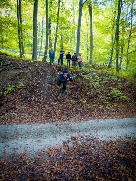 Person schwingt an Seil über einen Hang, Zuschauer stehen im Hintergrund