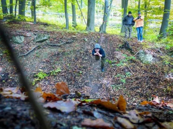 Person schwingt an Seil über einen Hang, zwei Personen beobachten