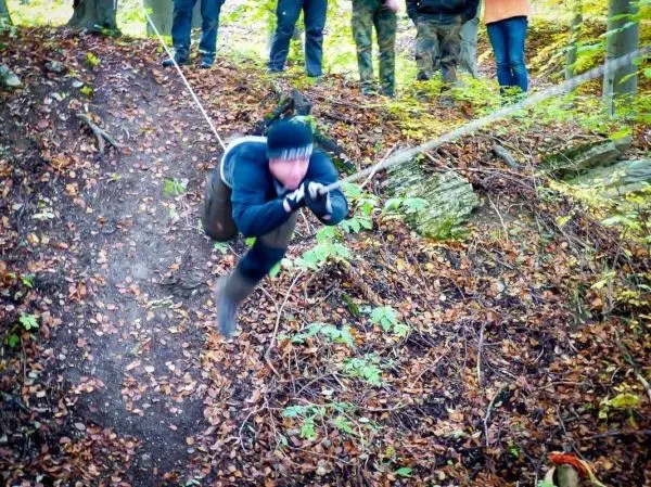 Person schwingt an Seil über einen steilen Hang im Wald