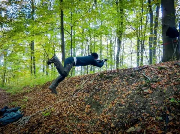 Person springt über eine selbstgebaute Seilbrücke im Wald