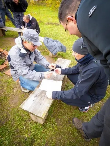 Personen besprechen etwas auf einer Holzbank beim Überlebenstraining