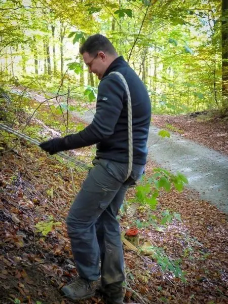 Seil wird an einem Baum befestigt, während der Boden mit Laub bedeckt ist