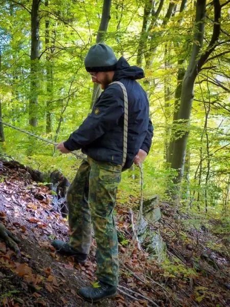Seil wird an einer Baumwurzel befestigt, während der Boden mit Laub bedeckt ist