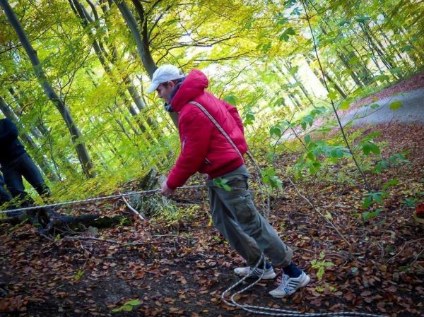 Seil wird durch den Wald gezogen, während ein Mann in roter Jacke zieht