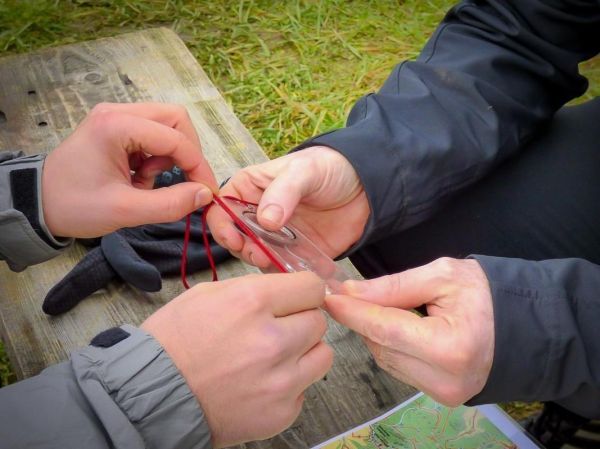 Zwei Hände justieren eine Kompassnadel auf einer Holzoberfläche